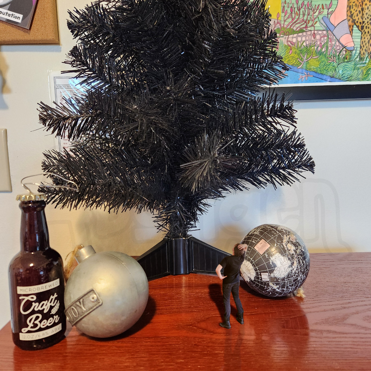 Tiny Aborigen stands at the base of a small tree, gazing up at it in perplexity. He is flanked by enormous spherical ornaments.