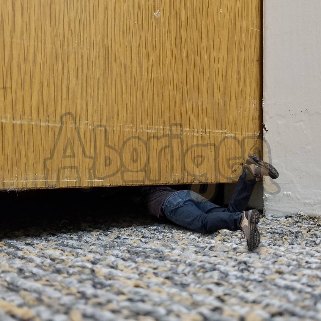 Tiny Aborigen crawls into the narrow gap between a heavy wooden office door and the industrial carpeting.