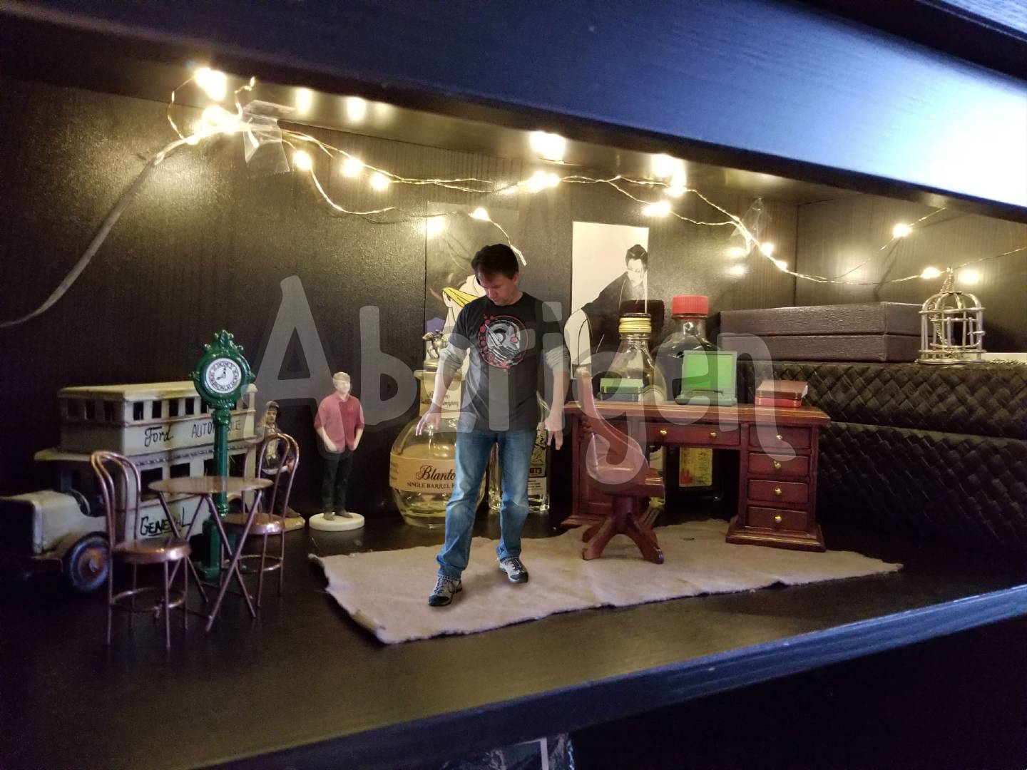 Tiny Aborigen stands in his writing studio, furnished with a miniature desk and chair and decorated with copper wire lighting and Patrick Nagel pictures clipped from a magazine.